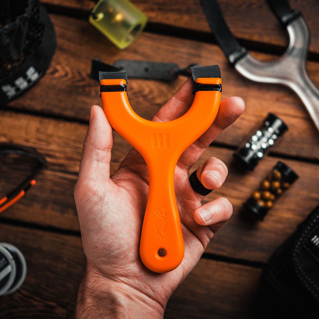 An orange Hornet slingshot held up in one hand over a wooden table