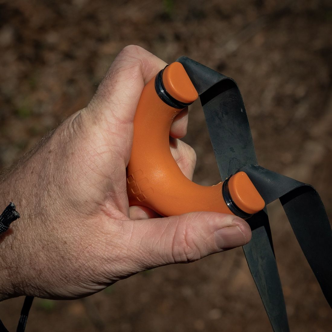 Hand holding an orange Sparrow slingshot with the bands drawn back along the forks
