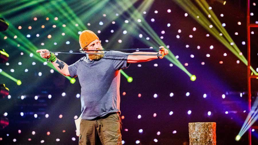 Zach Fowler on stage under green lights with a slingshot in hand