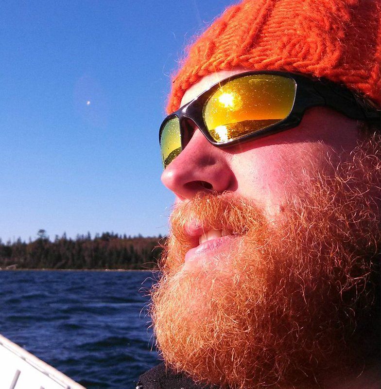 Close-up portrait of Zach Fowler in an orange beanie and mirrored sunglasses beside a lake